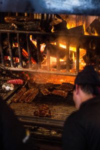 Parrilla de García Carrasco con cortes de carne sobre brasas y leña encendida.
