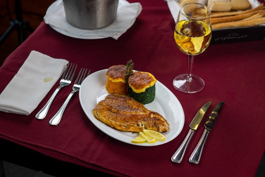 Plato de pesca fresca en García, con filete dorado y guarnición de verduras gratinadas, servido con limón.